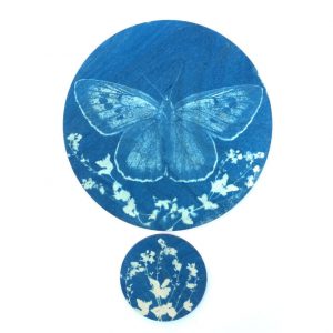 Blue butterfly on a wooden disc above a smaller wooden disc with floral design silhouette